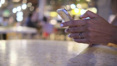 Bir kadın elinde bir cep telefonu tutuyor. Telefon bir restoranda bir masanın üzerinde. Kadın telefonuna odaklanmış, muhtemelen internete mesaj atıyor ya da internette geziniyor. Modern teknoloji kavramı