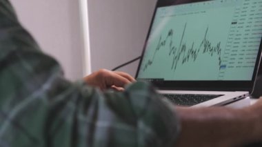 Bir adam dizüstü bilgisayarda yazıyor. Laptop grafiği gösteren bir ekrana açık. Adam ekrana odaklanmış, muhtemelen bir proje üzerinde çalışıyor ya da verileri analiz ediyor.