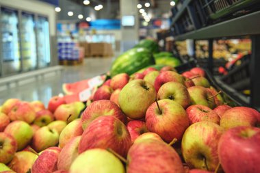 Elma ve avokado gibi tropikal meyveler taze ürünlerle dolu bir süpermarkette sergileniyor..