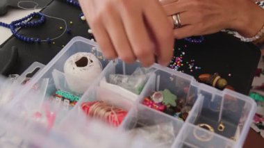 El yapımı mücevher, boncuk ve yaratıcı aletlerle dolu zanaatkar çalışma alanı. Çalışma alanı boncuklar, araçlar ve aksesuarlarla dolu, zanaatkârların kendini adamışlığı ve yaratıcılığı sergileniyor.