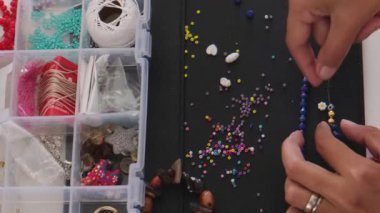 Küçük bir işletme sahibi, yaratıcı stüdyosunda eşsiz el yapımı mücevherler tasarlıyor ve yapıyor. Çalışma alanı boncuklarla, aletlerle ve aksesuarlarla dolu. Bu da zanaatkârların yaratıcılığını gösteriyor..