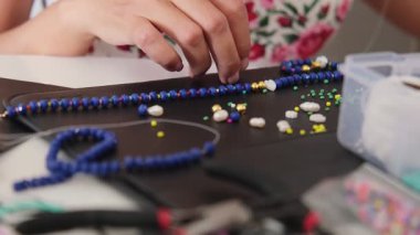 Küçük bir işletme sahibi, yaratıcı stüdyosunda eşsiz el yapımı mücevherler tasarlıyor ve yapıyor. Çalışma alanı boncuklarla, aletlerle ve aksesuarlarla dolu.