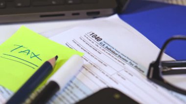 Vergi formu 1040, W-9, kalem, keçeli kalem, okuma gözlüğü ve dizüstü bilgisayar muhasebecilerin masasında.