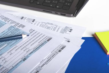 Vergi formu 1040, W-9, kalem, keçeli kalem, okuma gözlüğü ve dizüstü bilgisayar muhasebecilerin masasında.