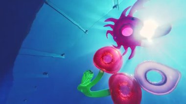 Pembe şişirilebilir yengeç ve çörek oyuncakları güneş ışığında mavi sularda yüzer, kabarcıklar yaratır ve yaz eğlencesi yaratır.