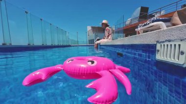 Pembe şişme yengeç, güneşli bir yaz gününde bir turist iskemlede dinlenirken mavi havuzun kenarında dinlenir.