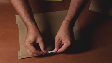 Zanaatkar dikkatlice çift taraflı bandı bir karton parçasına yapıştırıyor.