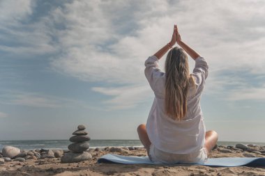 Ön planda bir yığın zen taşıyla plajda yoga yapan kadın.