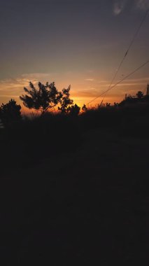 Sıcak turuncu ışık, güneş kıyı tepelerinin ardında batarken gökyüzünü aydınlatıyor.