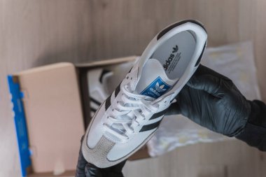 Eldivenli eller bir çift Adidas Samba spor ayakkabısı gösteriyor. Boks yaparken, ayakkabı ve kutu görünür.