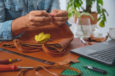Ayakkabıcı atölyesinde, aletler ve teknolojiyle çevrili iğne ve iplik kullanarak deri bir çanta dikiyor.