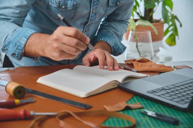 Deri ustası deftere not alıyor ve yeni deri eşyalar tasarlıyor.