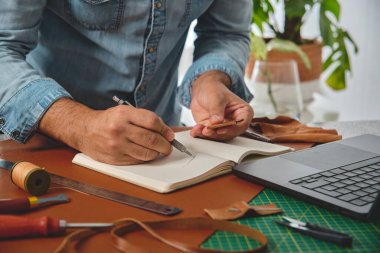 Deri ustası yeni deri ürünler için defterine çizimler çiziyor.