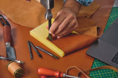 Çekiç ve dikiş aleti kullanan bir zanaatkar atölyedeki derinin üzerinde.