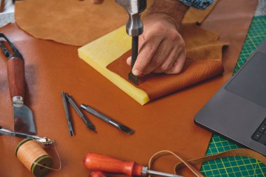 El sanatları ustası atölyesinde çekiç ve dikiş kamyonu kullanıyor. Etrafı alet ve dizüstü bilgisayarlarla çevrili.