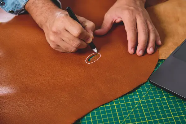 Zanaatkar atölyesindeki deri üzerine dizüstü bilgisayar ve kalem kullanarak resim çiziyor.