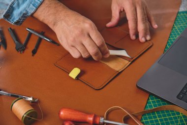 Ayakkabıcı atölyesinde el işi aletleri ve dizüstü bilgisayar kullanarak deriyle çalışıyor.