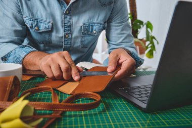 Deri işçisi atölyesinde cetvel ve dizüstü bilgisayar kullanıyor.