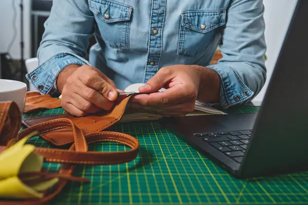 Deri ustası atölyede aletleri ve laptopuyla çalışıyor.