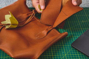 Esnaf, şık kahverengi deri bir çantanın parçalarını titizlikle bir tezgahın üzerinde birleştiriyor.