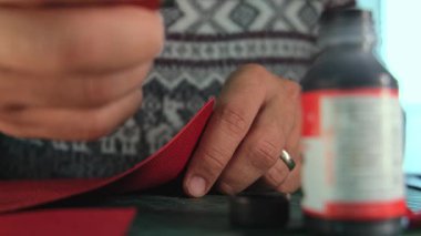 Deri ustası kırmızı deriye boyayı sürüyor.