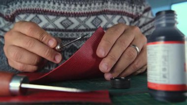 Kırmızı deride çalışan bir zanaatkar dikiş atarak delikler açıyor.