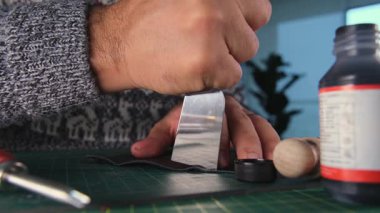 Zanaatkar, siyah boya ve aletle deri kenarı yakıyor.