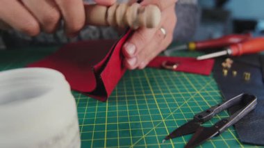 Deri ustası, ahşap bir aletle kırmızı deri üzerinde çalışıyor.