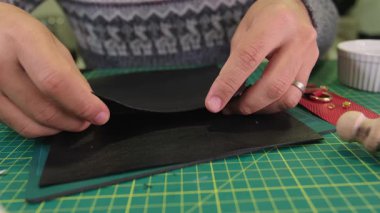 Deri ustası atölye masasına siyah deri yapıştırıyor.