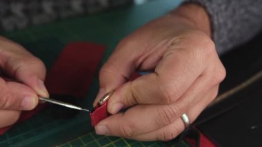 El sanatları ustası, kırmızı kumaşa deri bir çanta ile yapışkan sürüyor.