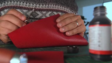 Zanaatkar kırmızı deri üzerinde çalışıyor, katlıyor ve tezgahı yapıştırıyor.