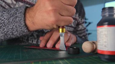 Zanaatkar döner bıçakla kırmızı deri kesiyor.