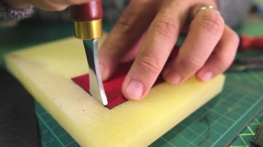 Deri ustası sarı bloknotta kırmızı deri kesiyor.