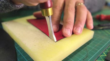 Deri ustası döner bıçakla kırmızı deri kesiyor.