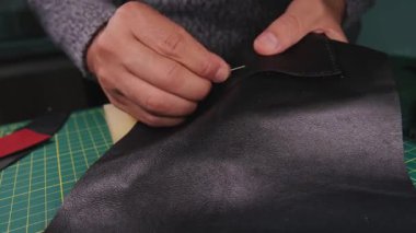 Deri ustası iğne ve iplik kullanarak siyah deri parçaları dikkatlice birleştiriyor.