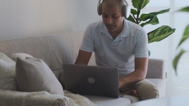 Kanepede dizüstü bilgisayar kullanarak evden uzakta çalışan odaklanmış bir çalışan.