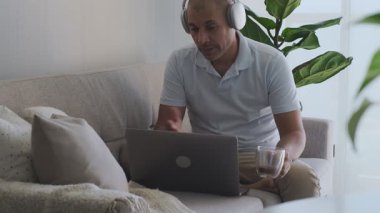 Evden kanepeye dizüstü bilgisayar ve kahveyle çalışan serbest çalışan biri.