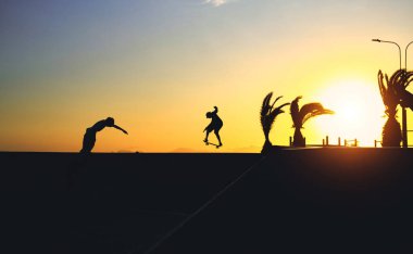 Kaykaylı patencinin arka plan gölgesi kaykay parkında gün batımında gökyüzünden atlarken, gün batımında sokakta kaykay yaparken..