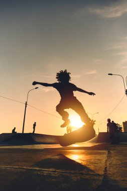 Kaykaylı patencinin arka plan gölgesi kaykay parkında gün batımında gökyüzünden atlarken, gün batımında sokakta kaykay yaparken..