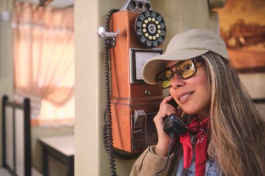 Eski bir ankesörlü telefondan telefon eden kadın turist, seyahatleri sırasında nostaljik bir anın tadını çıkarıyor.