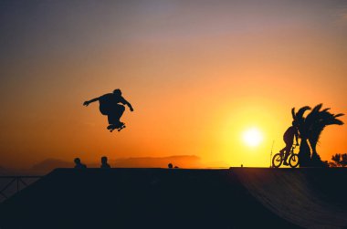 Kaykaylı patencinin arka plan gölgesi kaykay parkında gün batımında gökyüzünden atlarken, gün batımında sokakta kaykay yaparken..