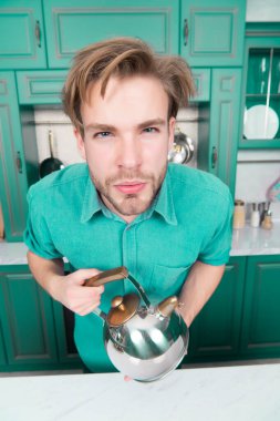 Oğlan mavi gömlekli ciddi yüzle su ısıtıcısı. Mobilya ve mutfak aletleri. Yiyecek hazırlama, pişirme, Isıtma, su kaynar. Çay zaman kavramı