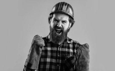 Çalışan aletleri olan bir inşaatçı. Vahşi, olgun hippi kareli gömlek ve sert şapka giyer. İşçi bayramı. Bina ve onarım. Yakışıklı işçi adam. Üniformalı eldivenli erkek işçi. Onarım için araçlar.