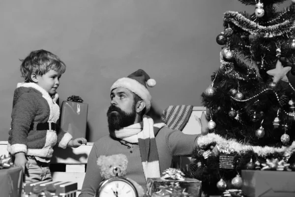 家族の休日のコンセプトです クリスマスの家族は 緑の背景にお互いを見る ひげと息子を果たしていること好奇心が強い面を持つ男 サンタとクリスマス ツリーの近くのギフト ボックスの中で小さなアシスタント — ストック写真