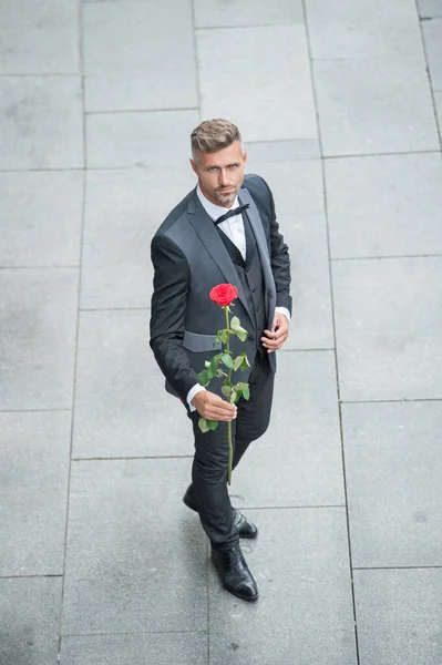 elegant man in tuxedo. man wearing bowtie suit outdoor. handsome tuxedo man with red rose. full length.