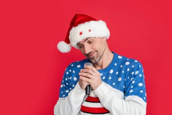 christmas song. shy man singing christmas song with microphone in studio. man singing christmas song isolated on red background.