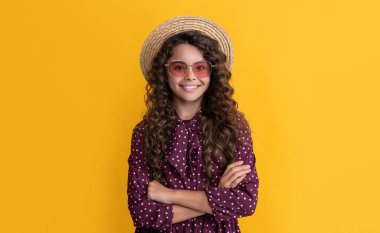 smiling child in straw hat and sunglasses with long brunette curly hair on yellow background. clipart