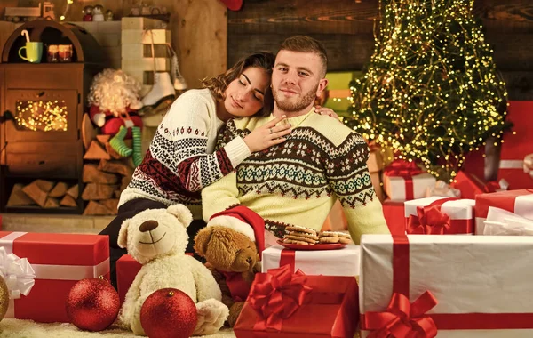 Couple in love sitting next to Christmas tree. hugging among present boxes. romantic couple is having fun. evening before xmas. Enjoying spending time together in New Year Eve.