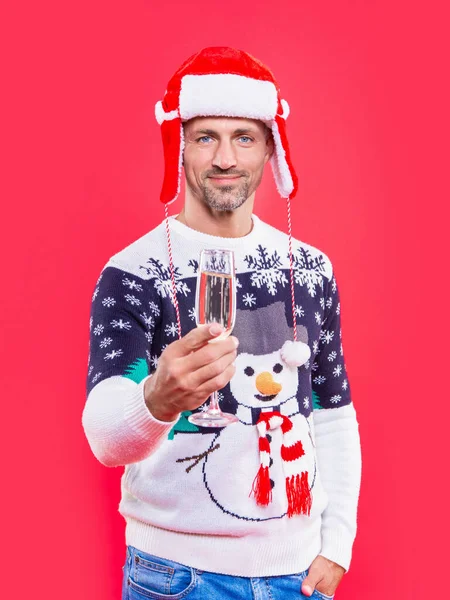 man in christmas earflap hat cheering with champagne. christmas man isolated on red background. man hold champagne for christmas in studio. christmas champagne and man in sweater.