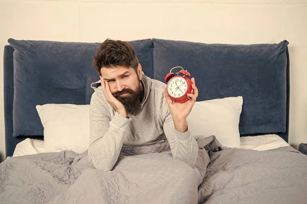 Sleepy man holding alarm clock being in bed in morning, time.